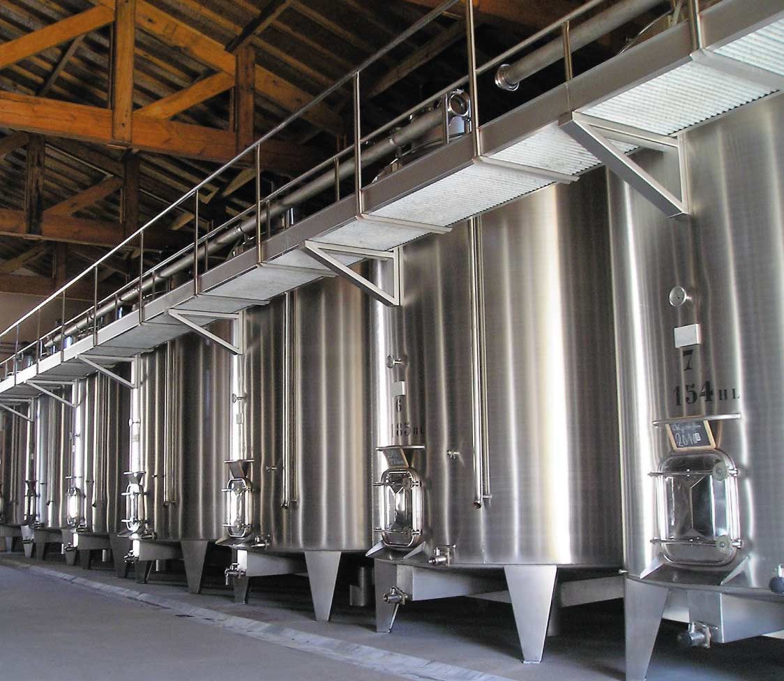 Row of large stainless steel tanks in Château Saint Hilaire winery, with a metal walkway above.