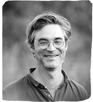 Man with glasses smiles, outdoors.