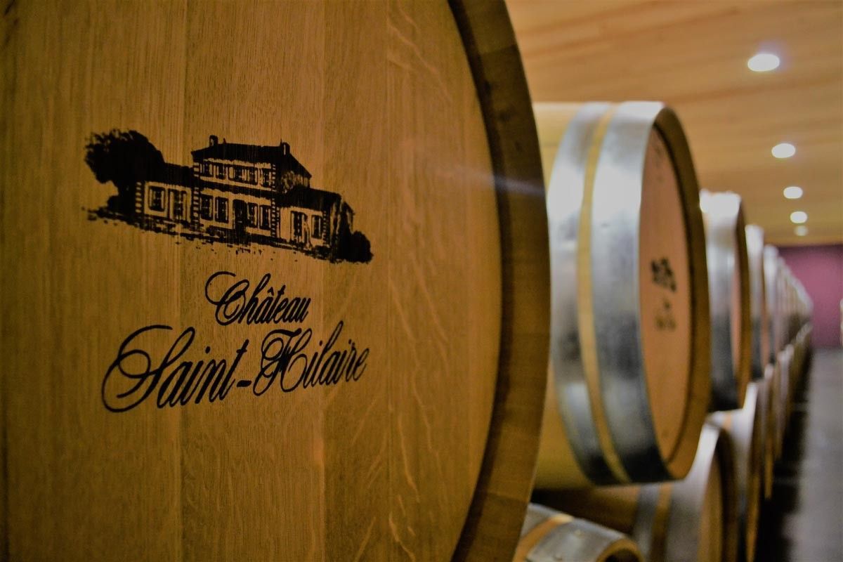 Wooden wine barrels in a cellar, with the Château Saint Hilaire logo