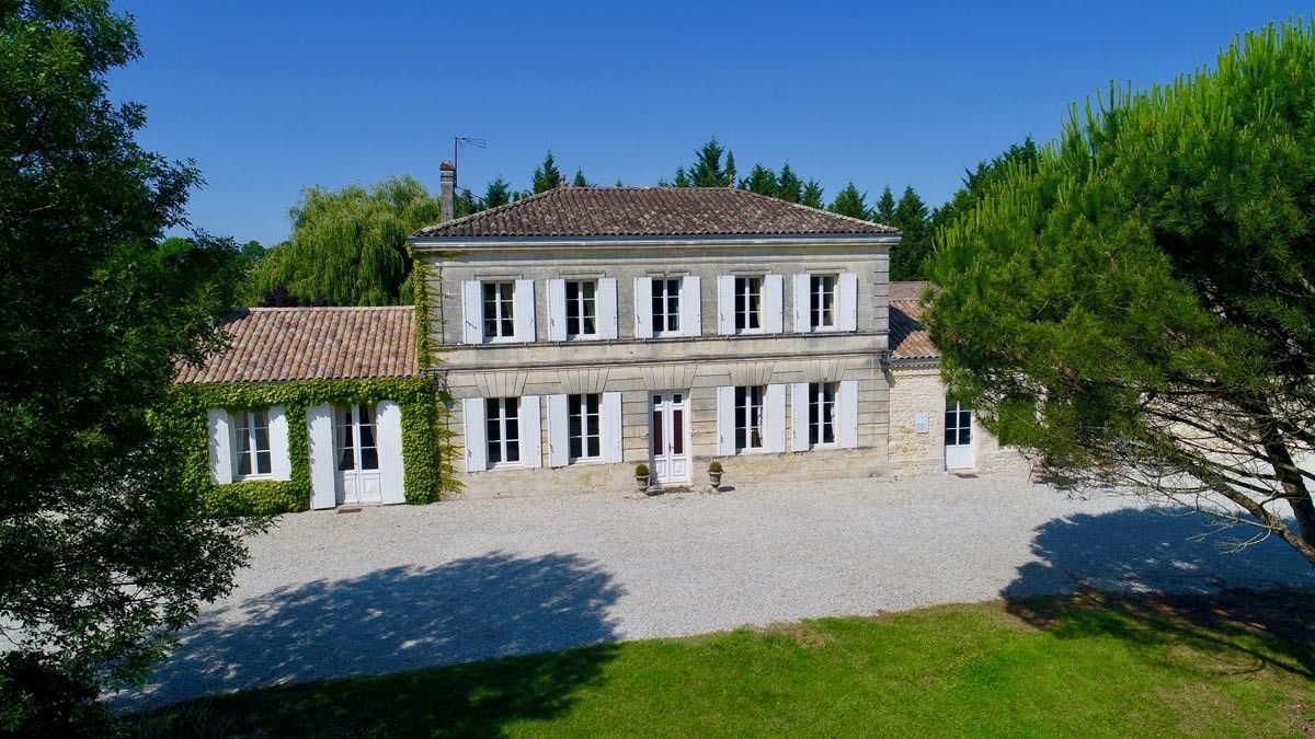 Two-story stone house with white shutters, red-tiled roof, and a gravel driveway at Château Saint Hilaire