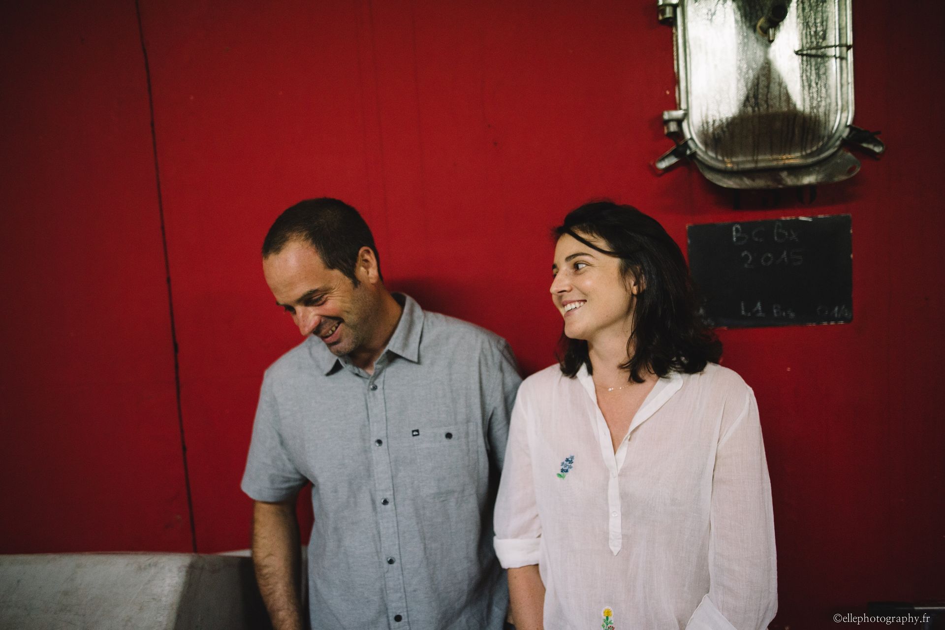 Winemakers of Peybonhomme-les-Tours smiling, leaning against a red wall.