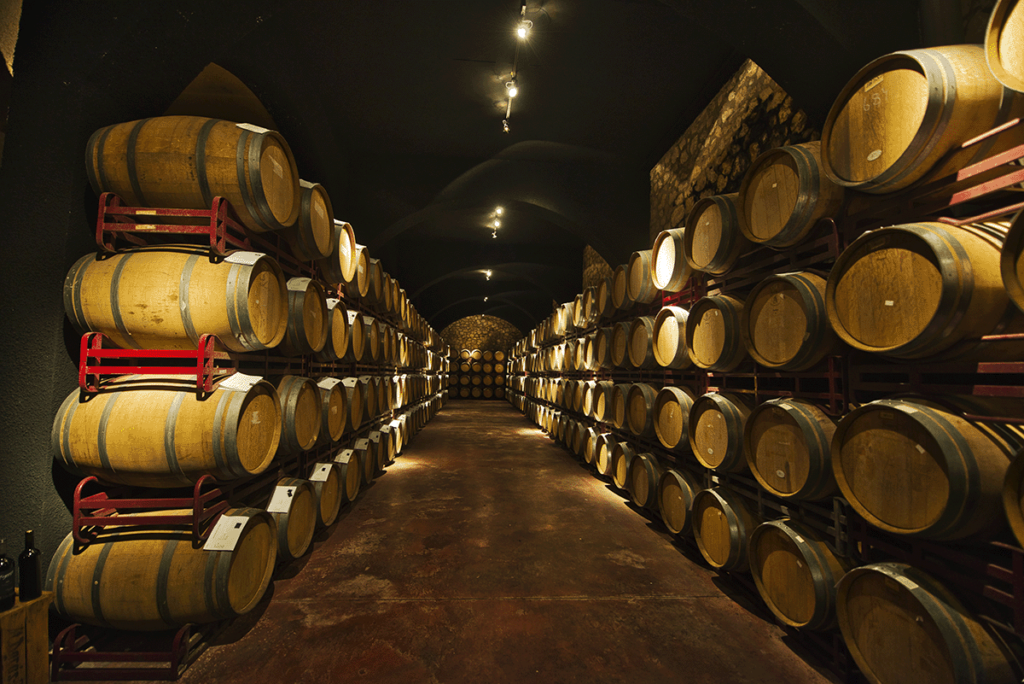 Rows of wooden wine barrels in a dimly lit cellar, at Bodegas Enguera