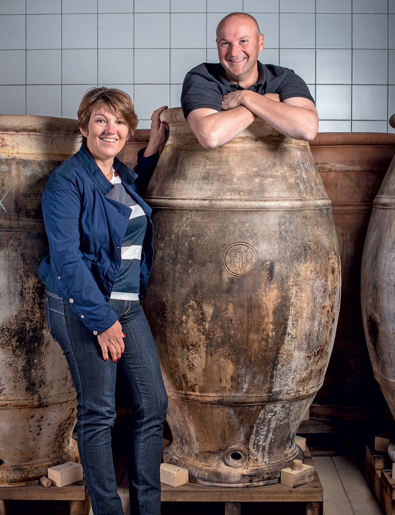 Winemakers of Tissot posing by large, weathered amphorae in a cellar-like room.