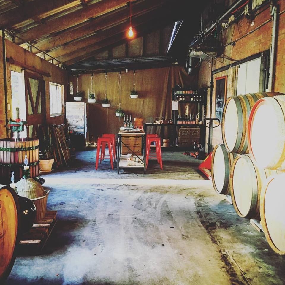The interior of the Unico Zelo winery, showing oak barrels, winemaking equipment, and a rustic tasting area.