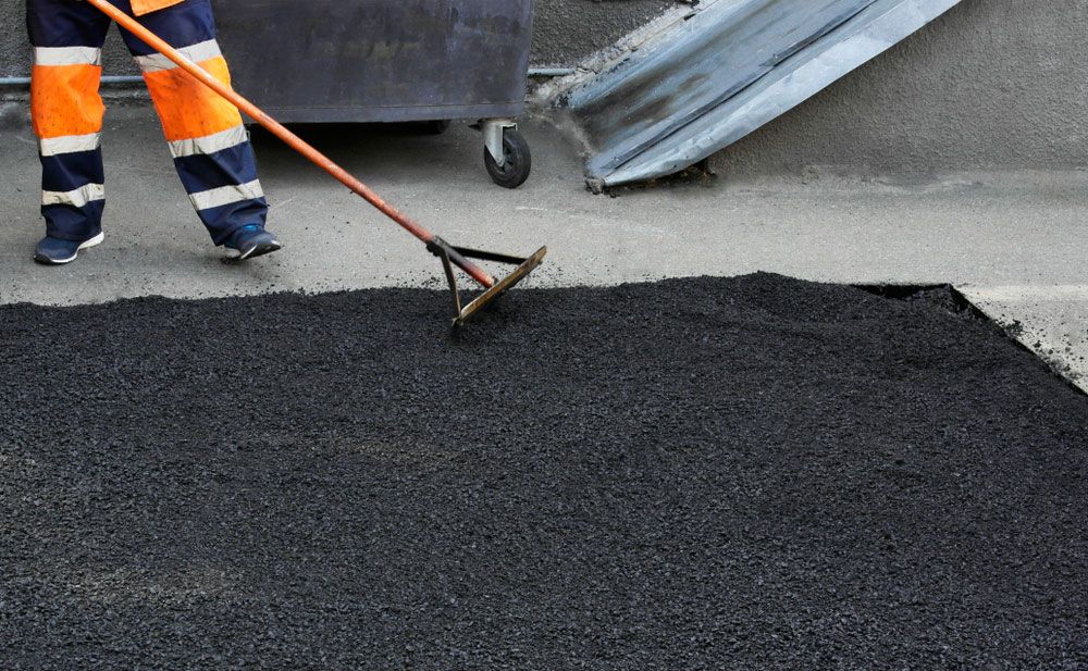 A Man Is Raking A Pile Of Asphalt On The Ground — East Point Earthmoving in Brunswick Head, NSW