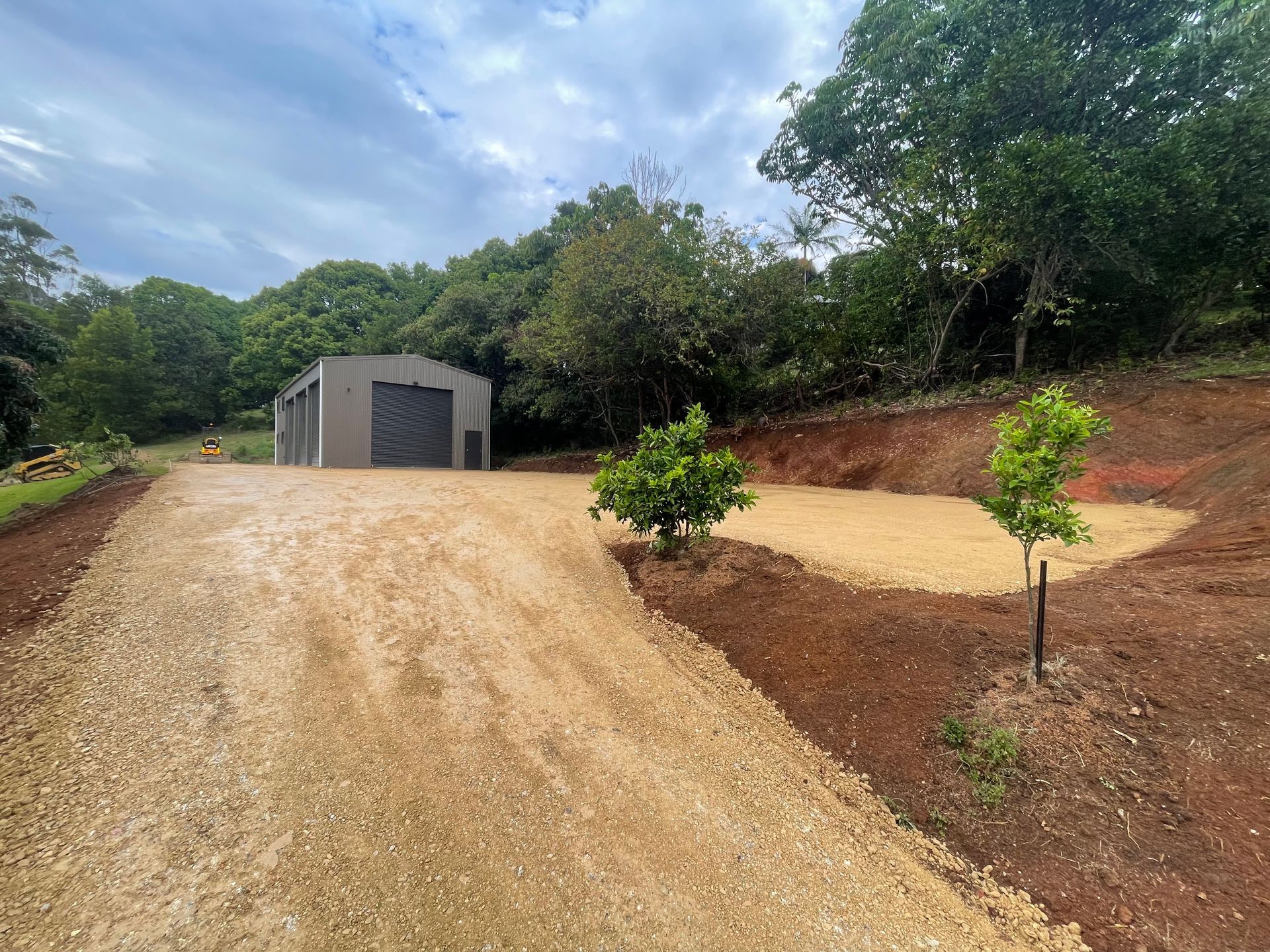 A Small Orange Excavator Is Sitting On A Dirt Road — East Point Earthmoving in Byron Bay, NSW