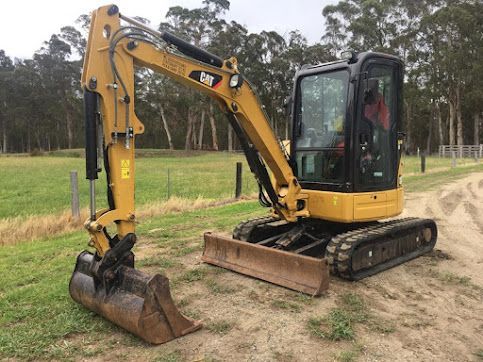 A Small Yellow Excavator Is Parked On The Side Of A Dirt Road — East Point Earthmoving in Bangalow, NSW