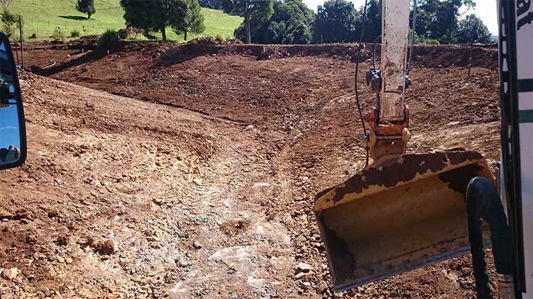 A Bulldozer Is Moving Dirt On A Muddy Road — East Point Earthmoving in Byron Bay, NSW
