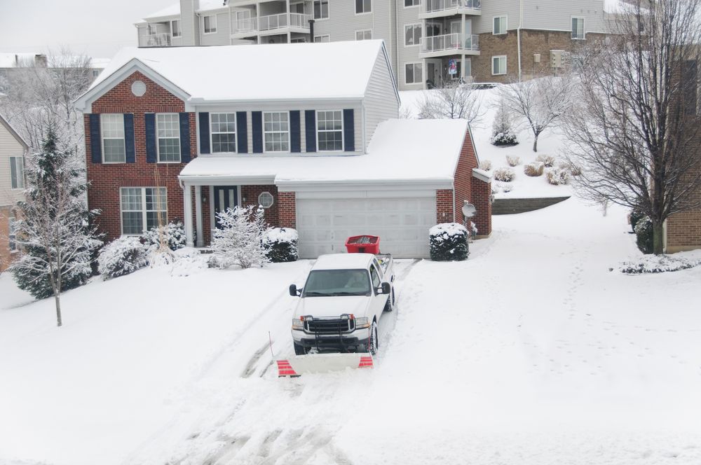 A snow plow is clearing a driveway in front of a house