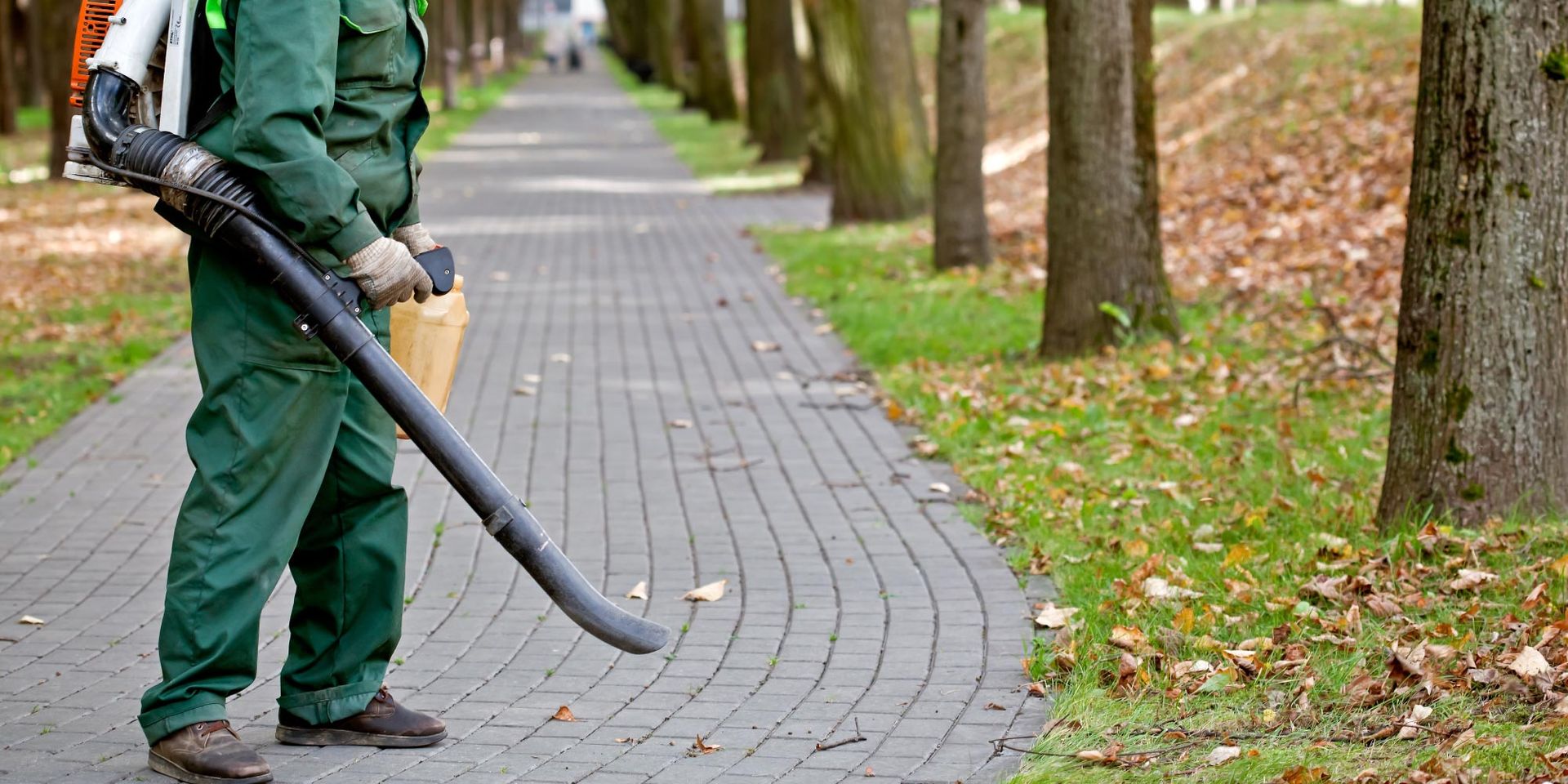 A man is standing on a sidewalk using a leaf blower.
