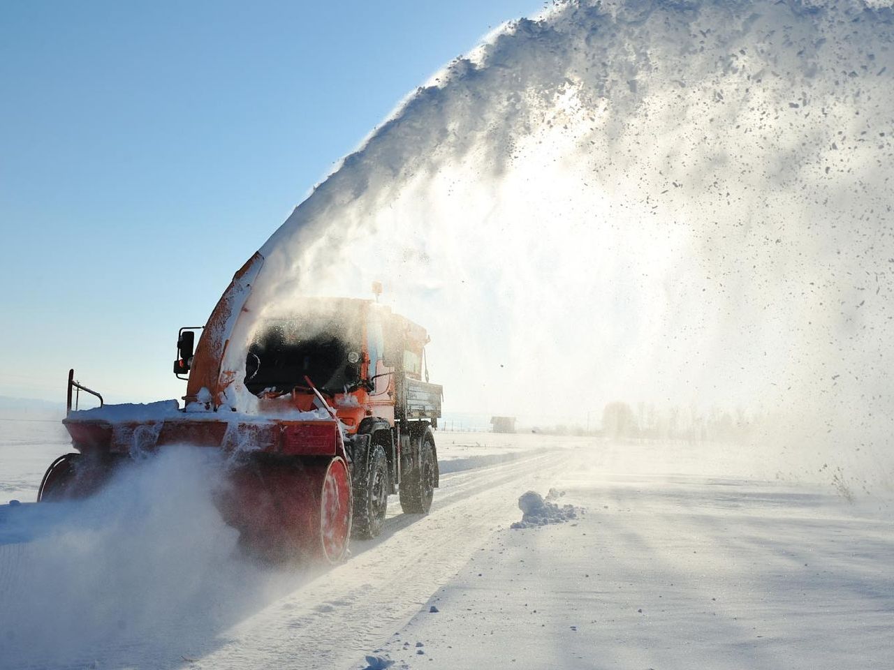 A snow blower is blowing snow on a snowy road.