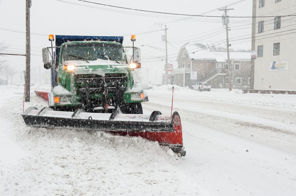 A snow plow is driving down a snowy street.