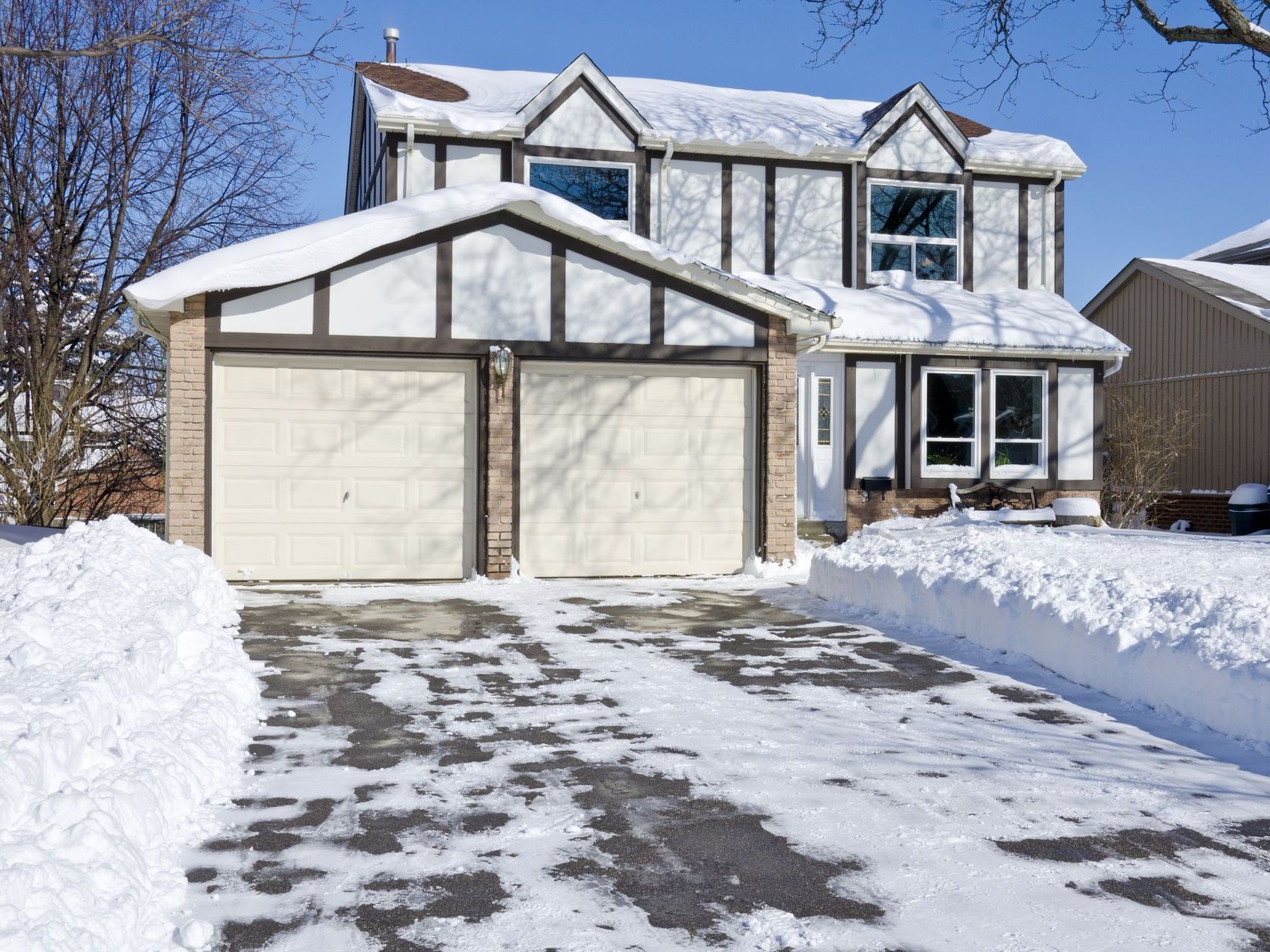 A house with two garage doors and a driveway covered in snow.