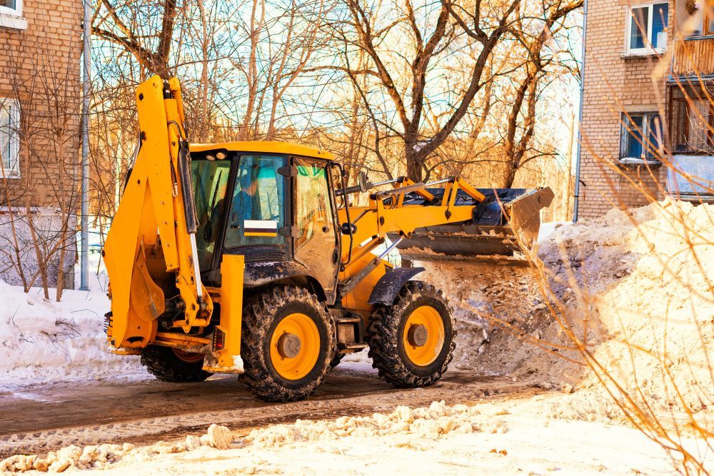 A yellow bulldozer is clearing snow from a street in front of a building.