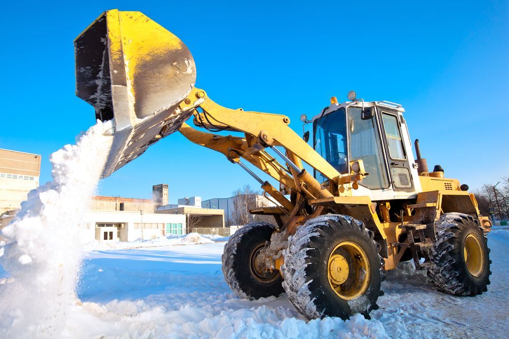 A yellow bulldozer is clearing snow from a parking lot.