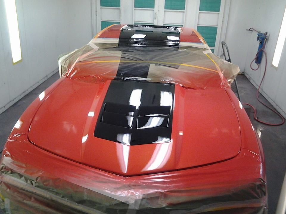 A red car is being painted in a paint booth.