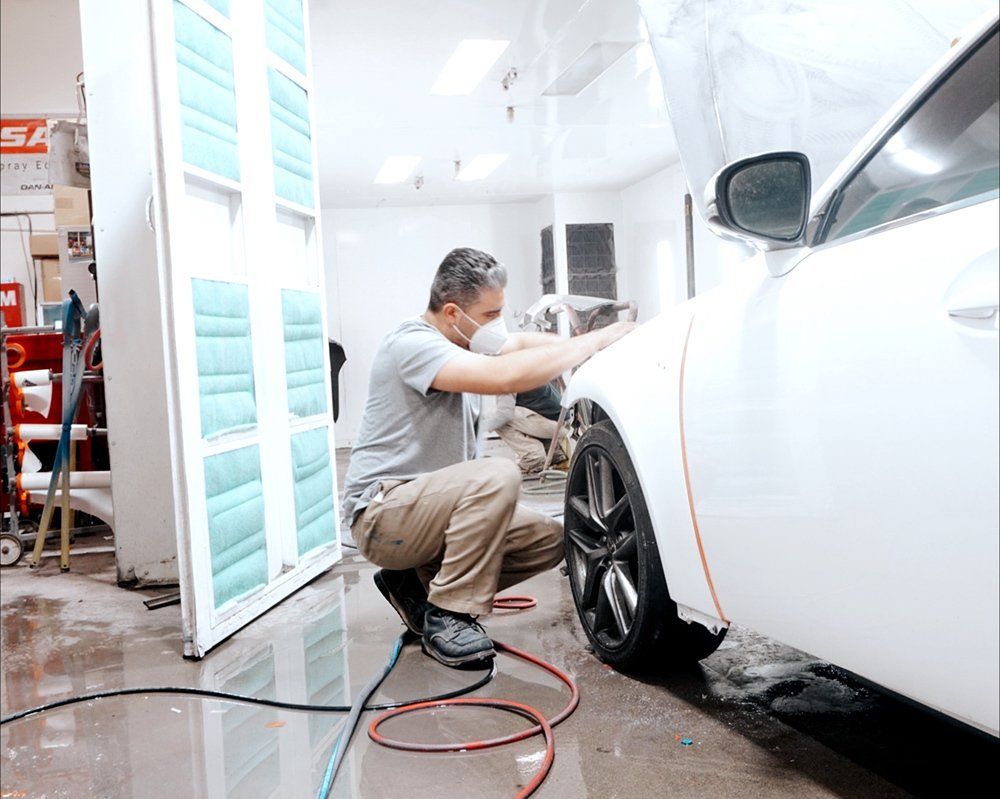 A man is kneeling down next to a white car in a garage.