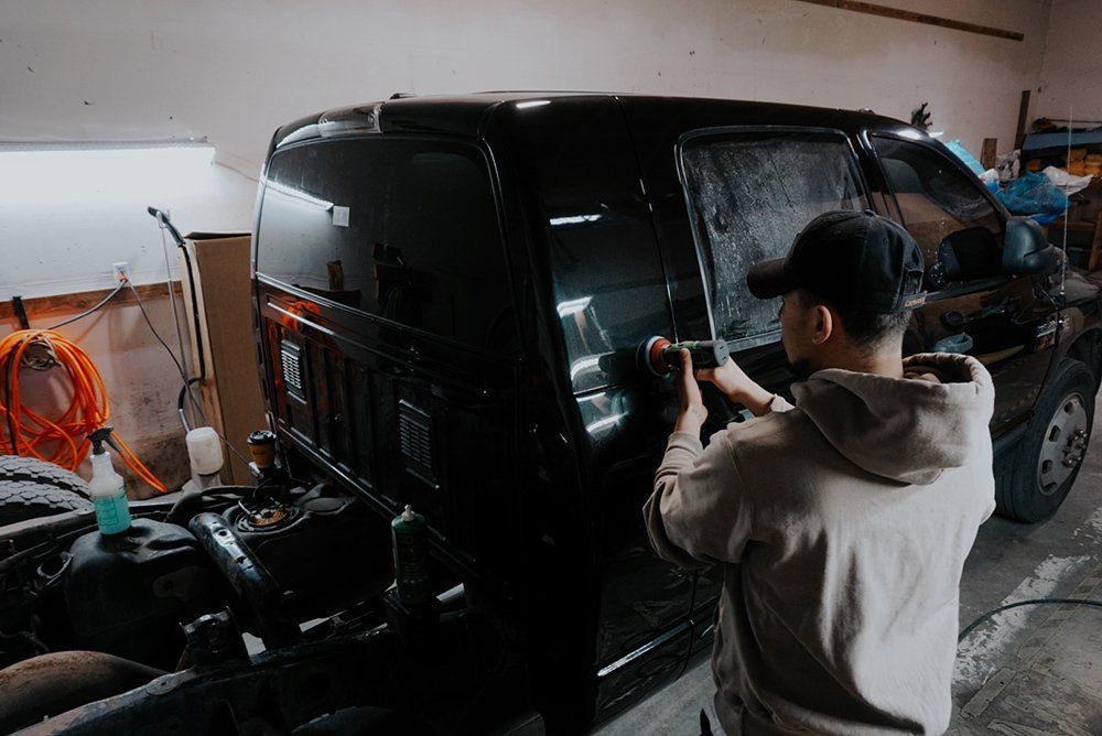 A man is standing next to a black van in a garage.