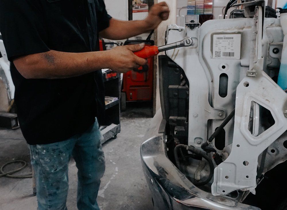 A man is working on a car with a screwdriver.
