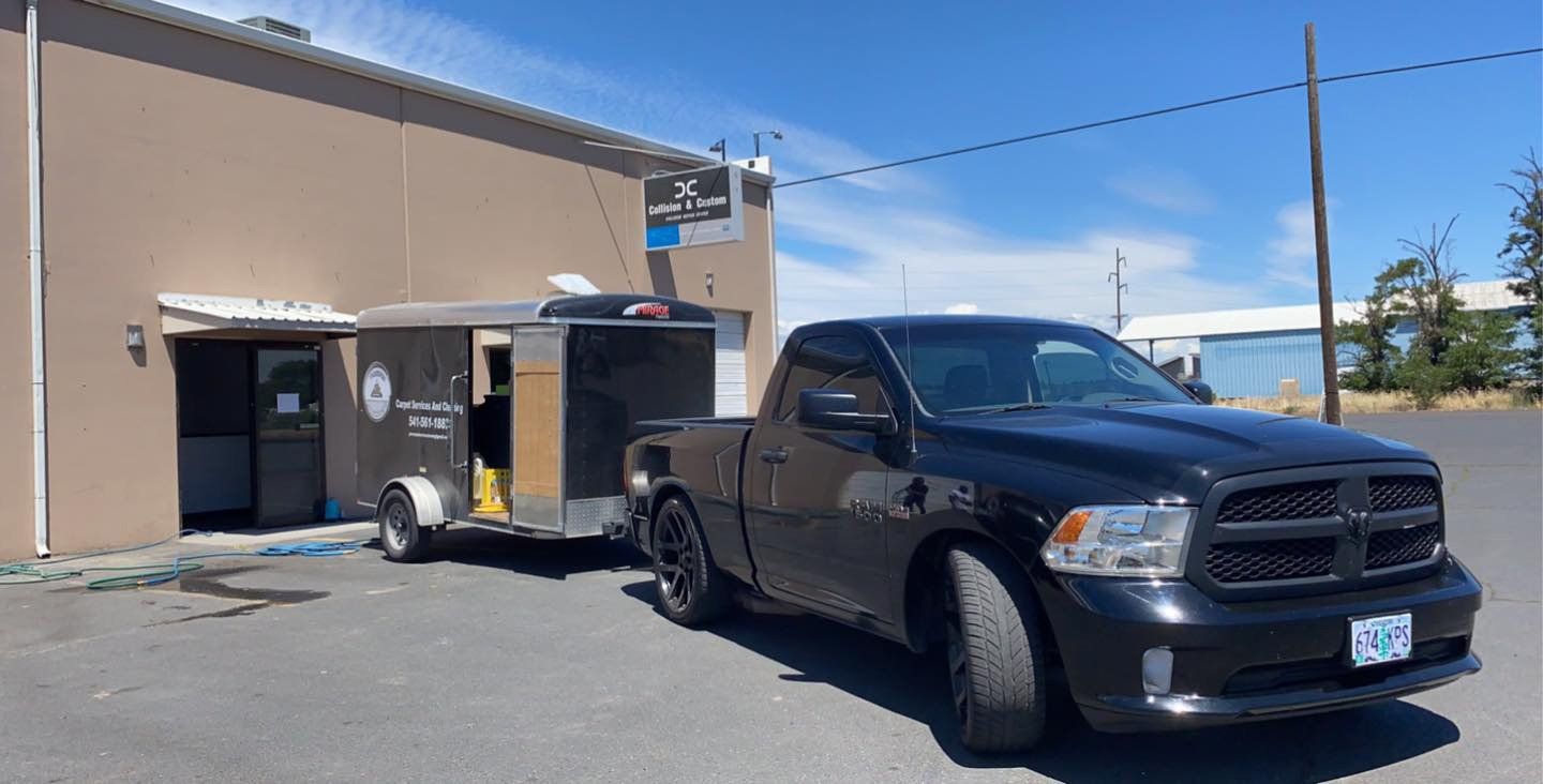 A black truck with a trailer attached to it is parked in front of a building.