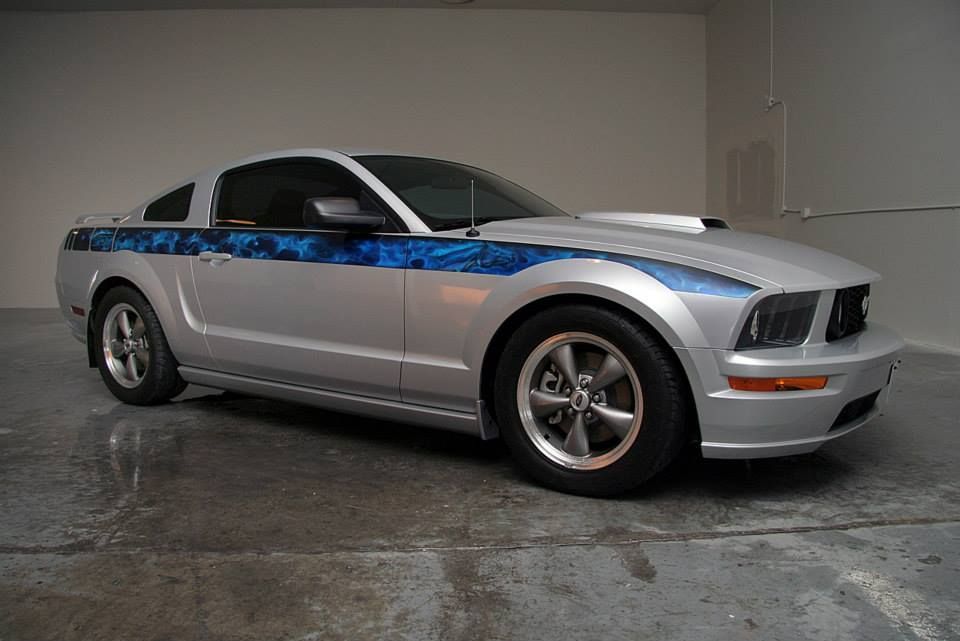 A silver mustang with blue stripes is parked in a garage.