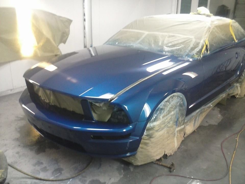 A blue car is being painted in a garage