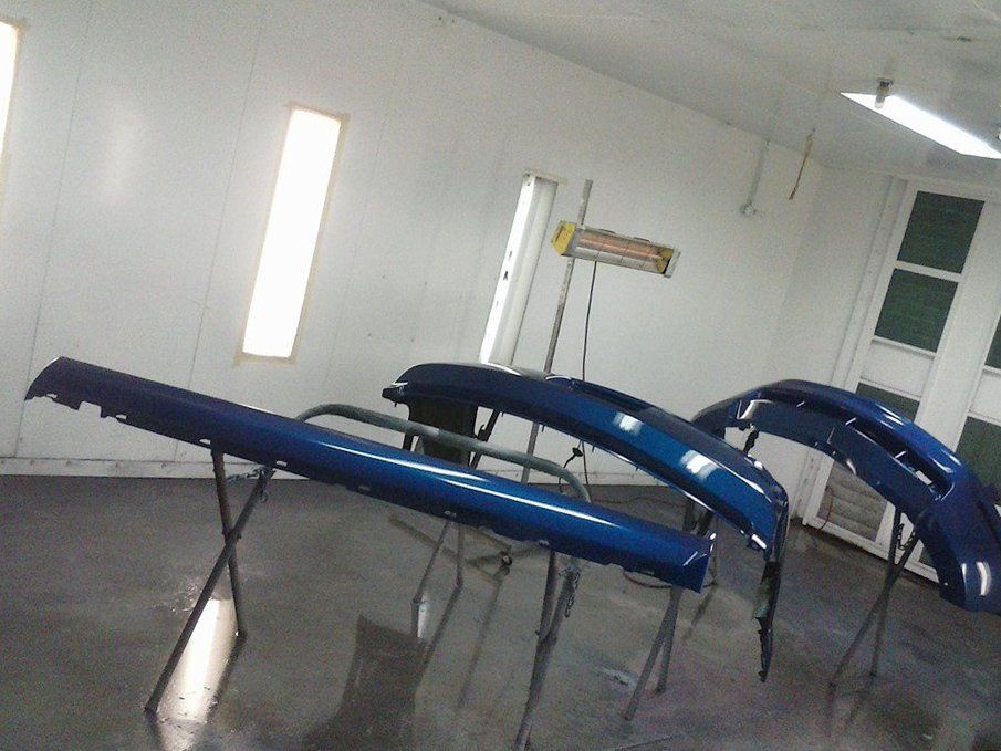 A row of blue bumpers are sitting in a paint booth