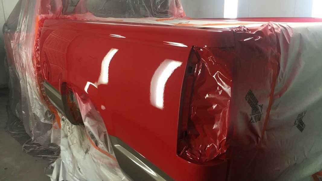 A red truck is being painted in a garage.