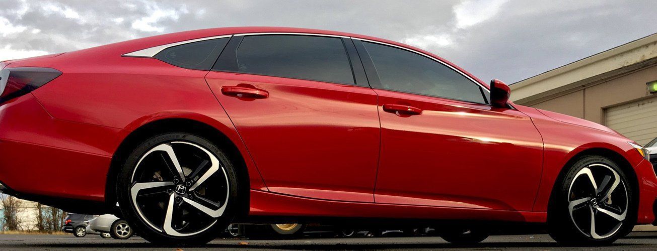 A red car with black wheels is parked in front of a building.