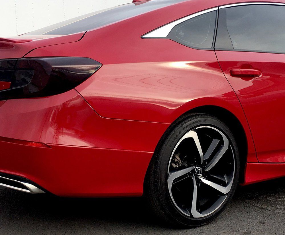 A red car with black wheels is parked on the side of the road
