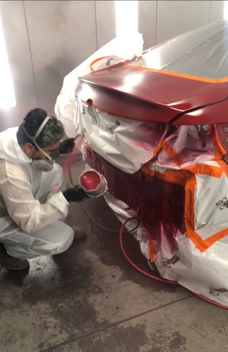 A man is painting a red car in a paint booth.