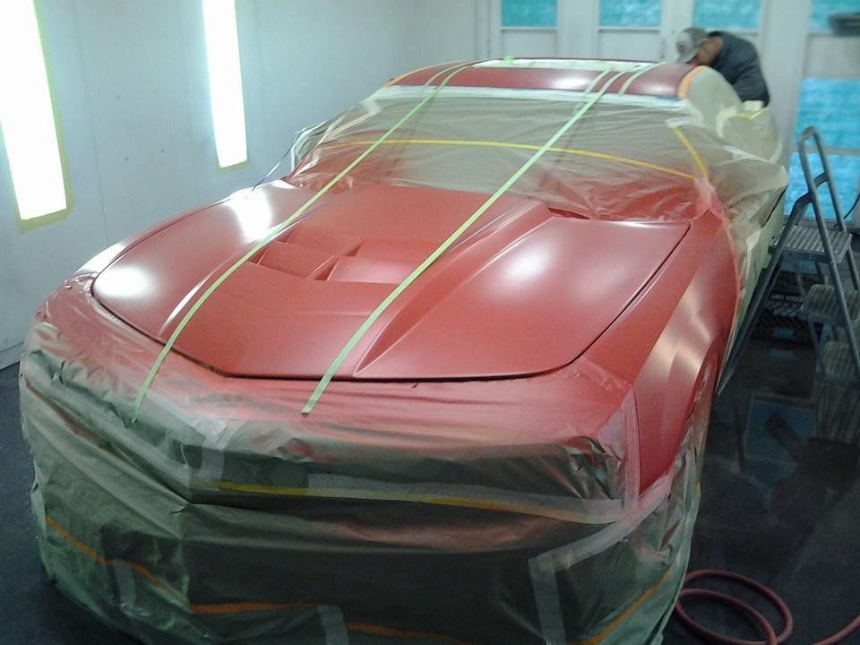 A red car is being painted in a paint booth