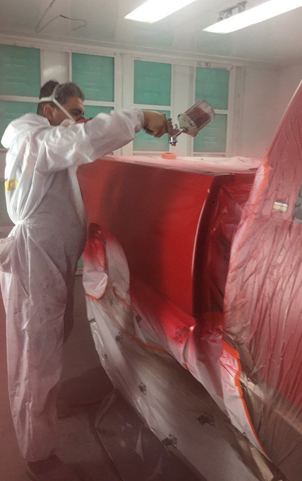 A man is painting a red car in a paint booth.