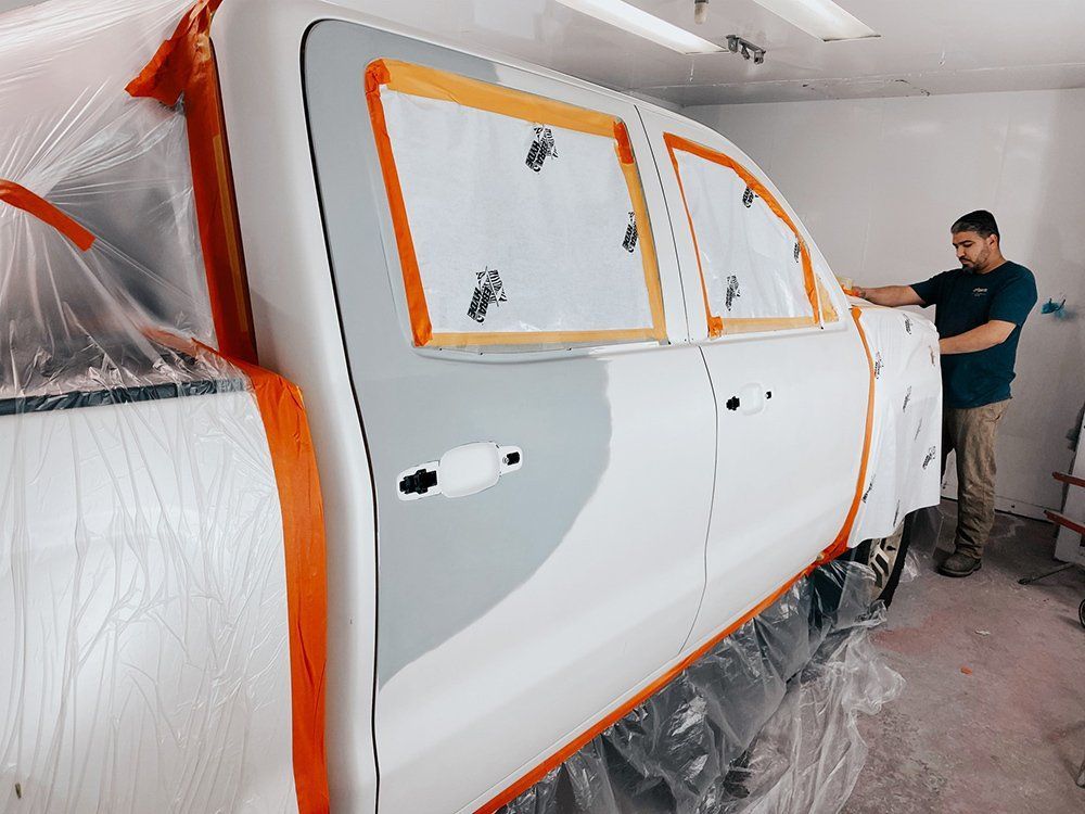 A man is painting a white truck in a garage.