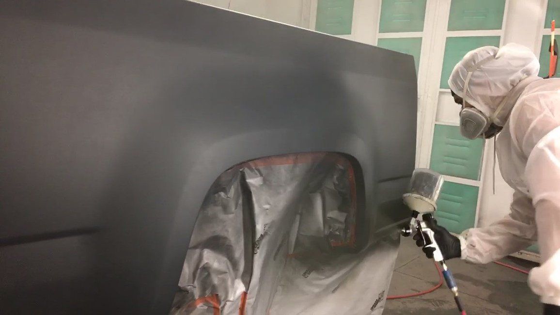 A man is spray painting a truck in a paint booth.