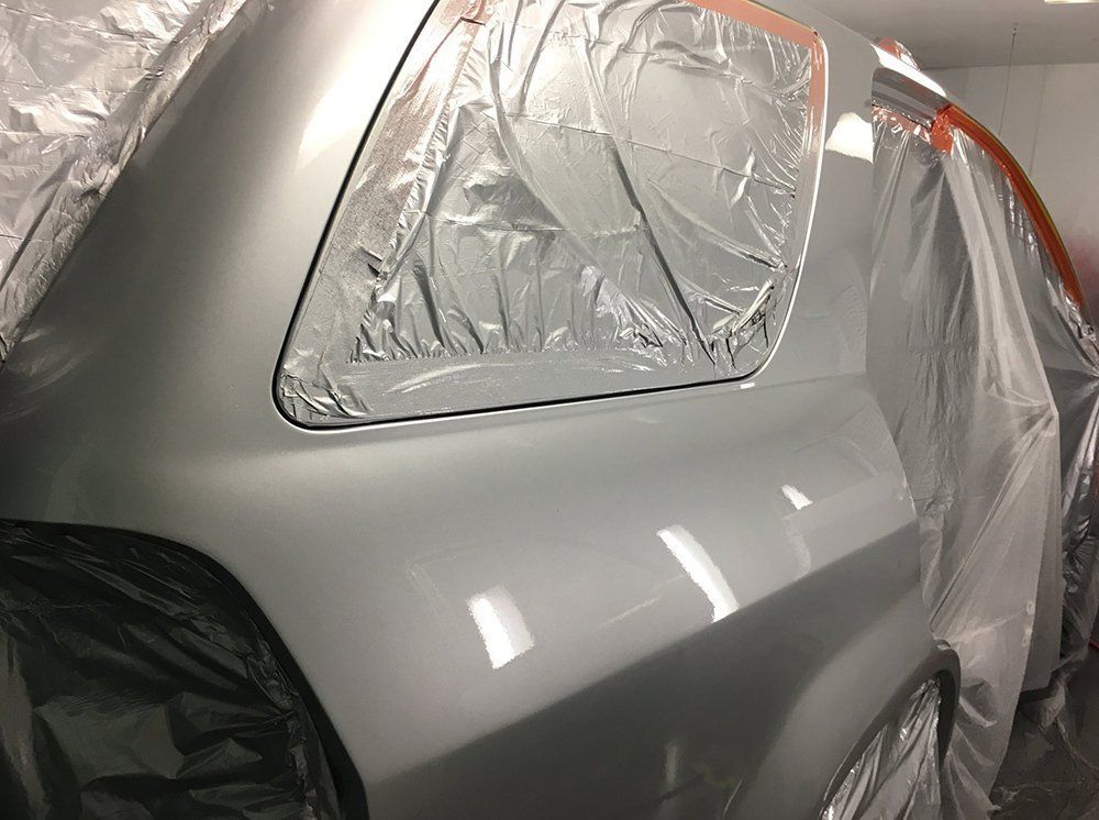 A silver car is covered in plastic and is being painted.