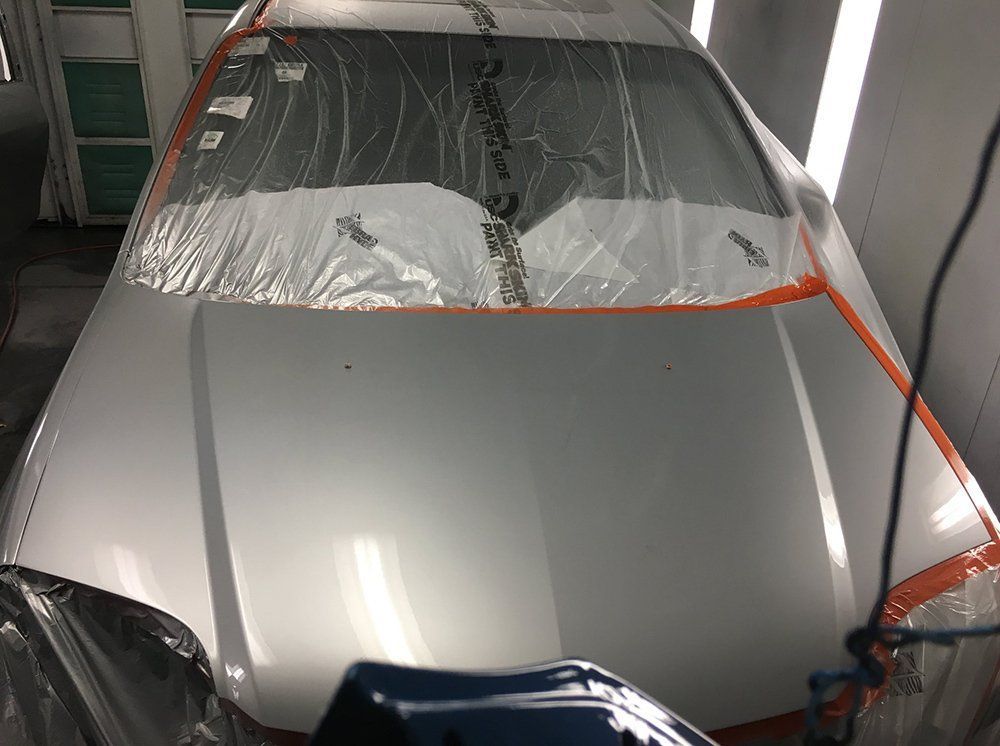 A silver car is being painted in a paint booth.