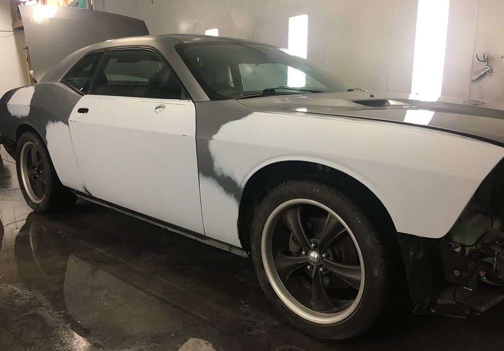 A white dodge challenger is being painted in a garage.