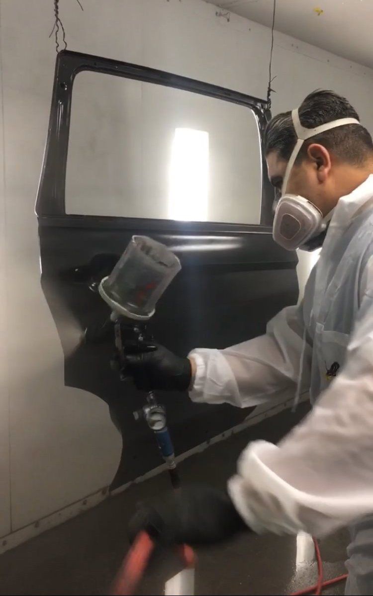 A man wearing a mask is spray painting a car door.