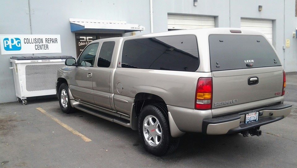 A gmc truck is parked in front of a building that says collision repair