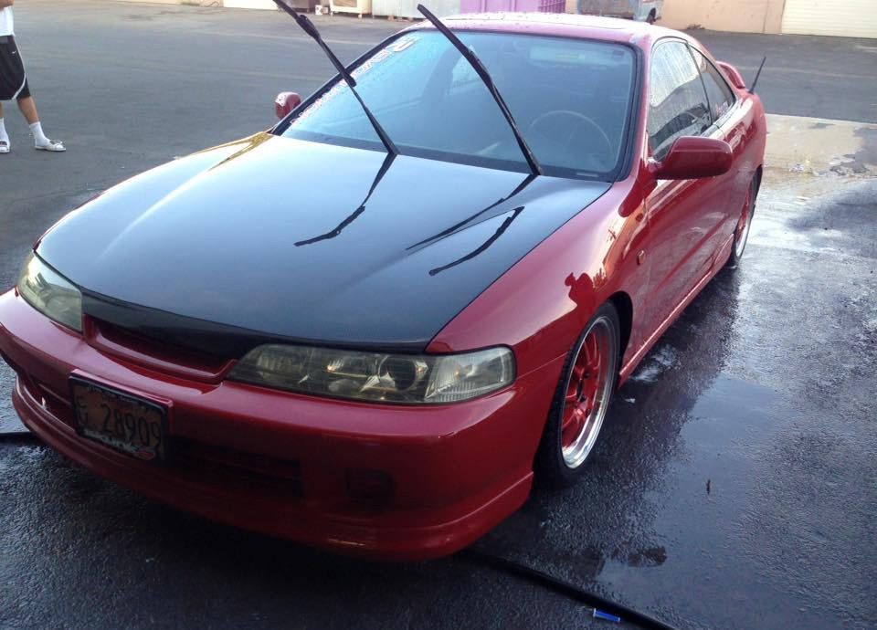 A red car with a black hood is parked in a parking lot