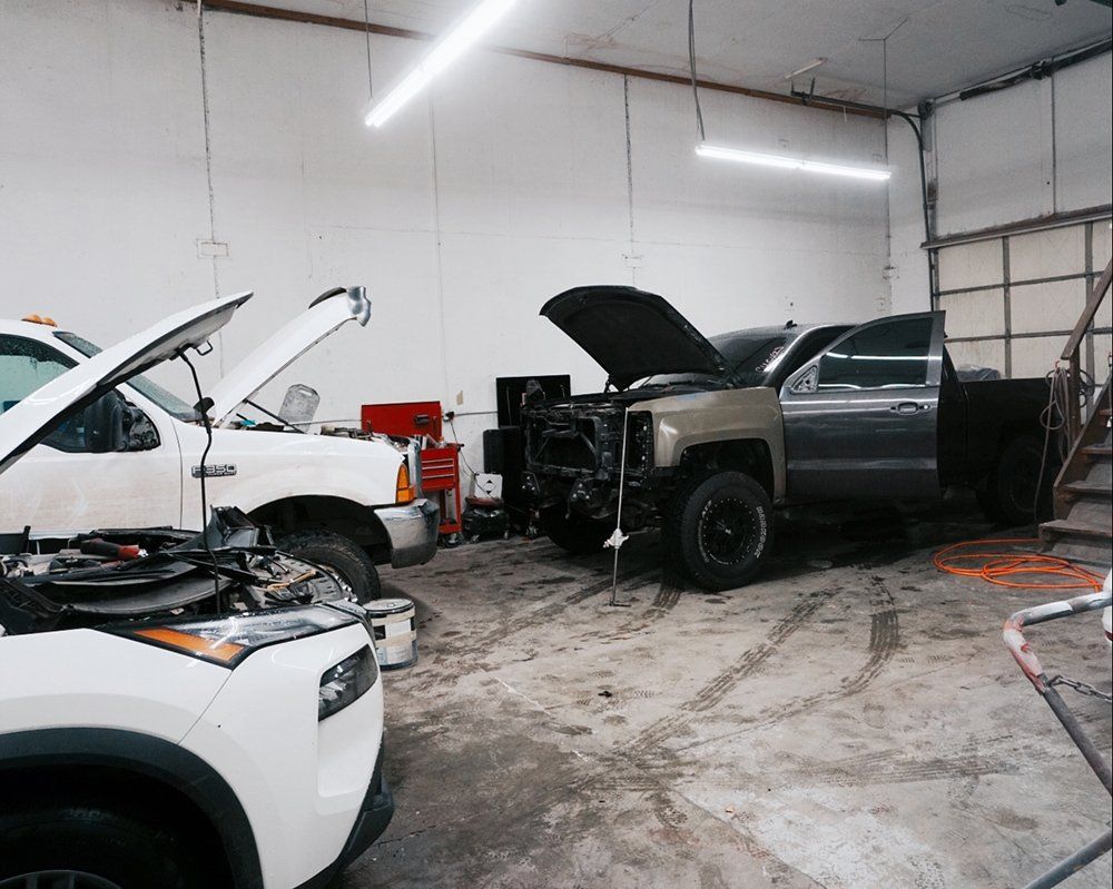 Two trucks are in a garage with their hoods open.