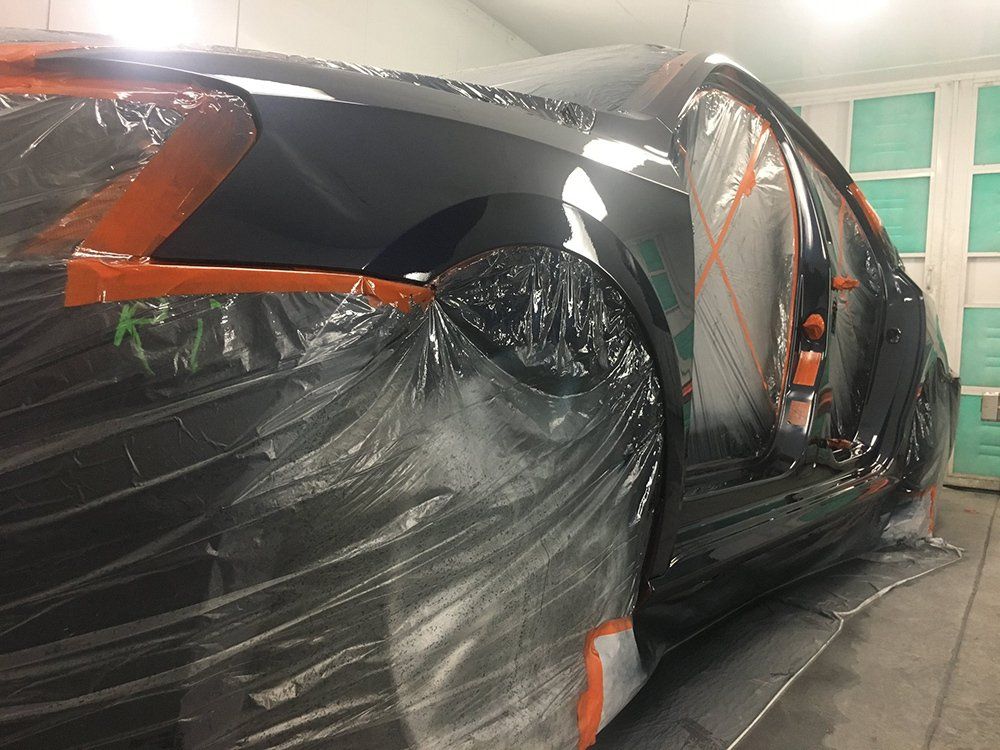 A black car is covered in plastic while being painted in a garage.