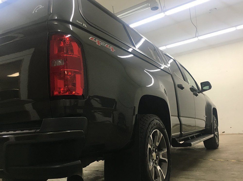 A black truck with a red tail light is parked in a garage.