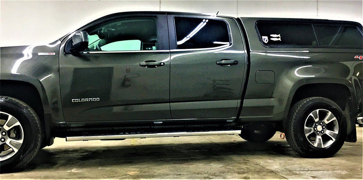 A gray truck with a canopy is parked in a garage.