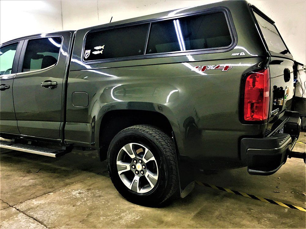 A green truck with a canopy is parked in a garage.