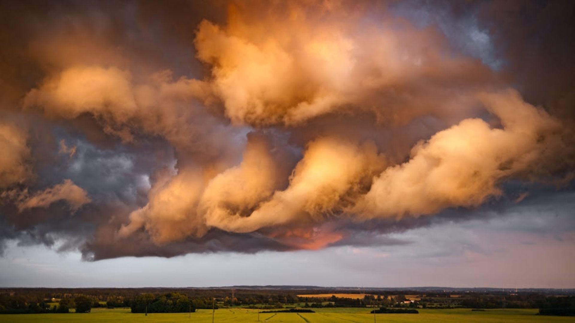 Nubes de tormenta iluminadas de color naranja sobre un paisaje verde llano al atardecer.
