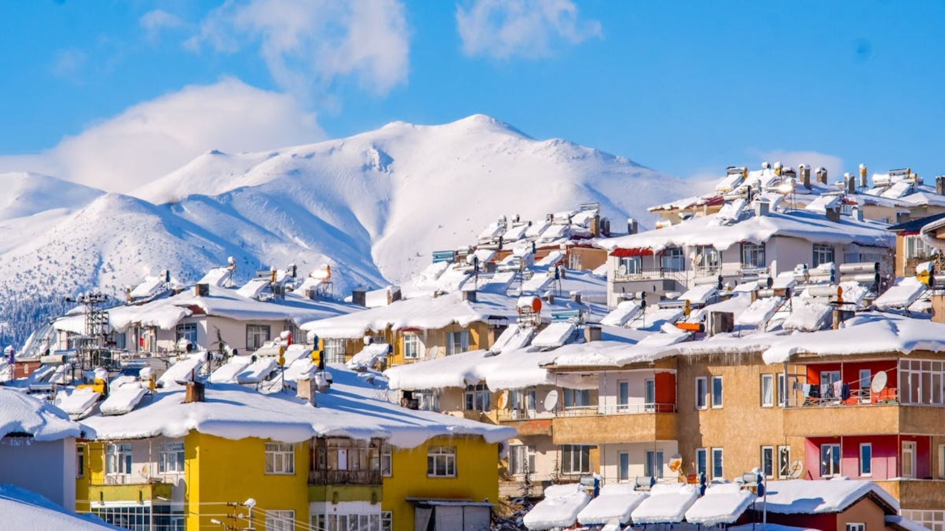Edificios cubiertos de nieve con paneles solares, enclavados contra montañas nevadas bajo un cielo azul.