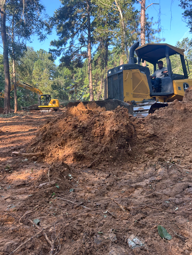 Dump truck dumping soil onto a dirt pile in a grassy yard, under a blue sky.