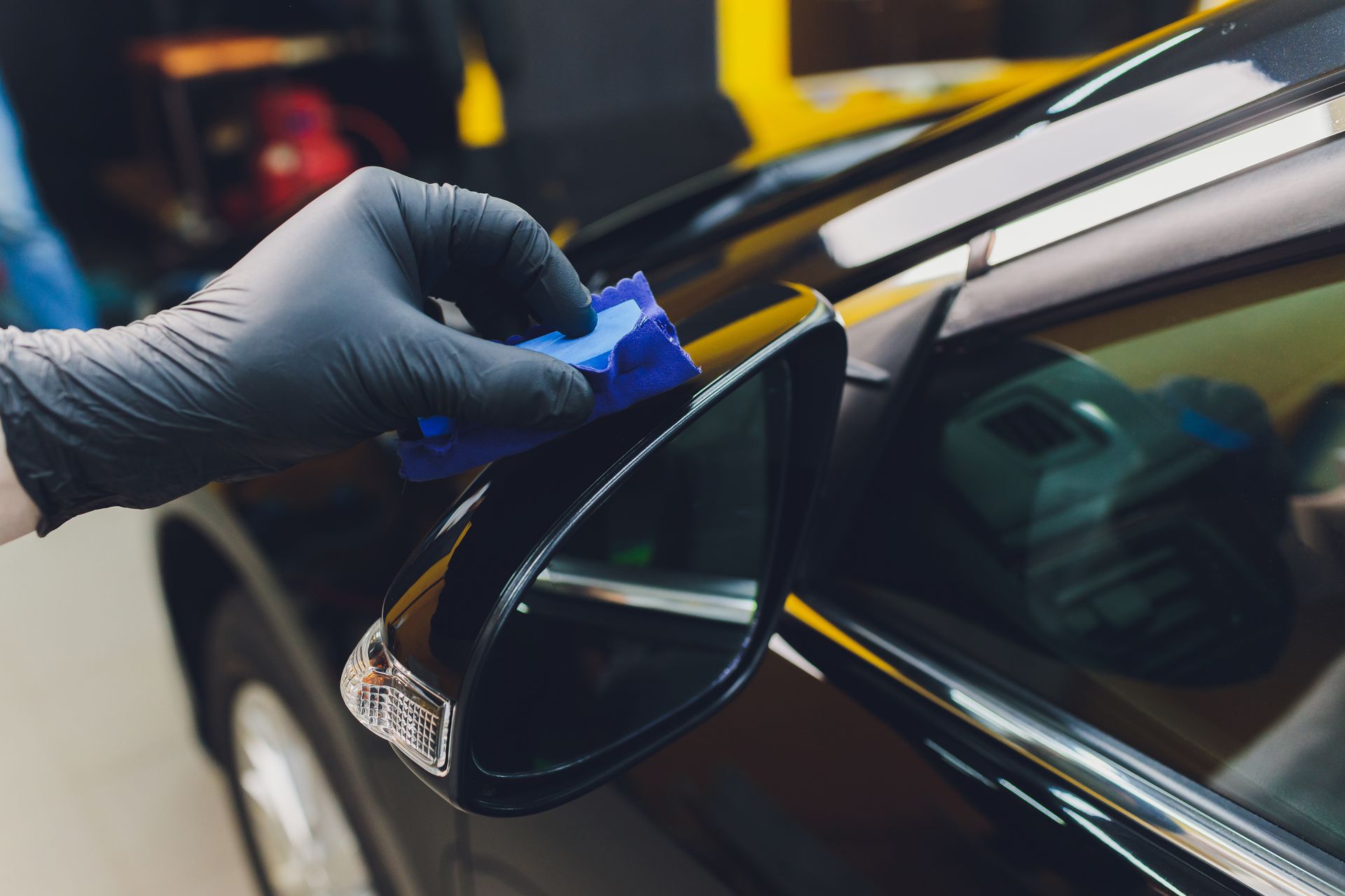 Gloved hand applying blue tape to a car’s rear window edge at an auto shop